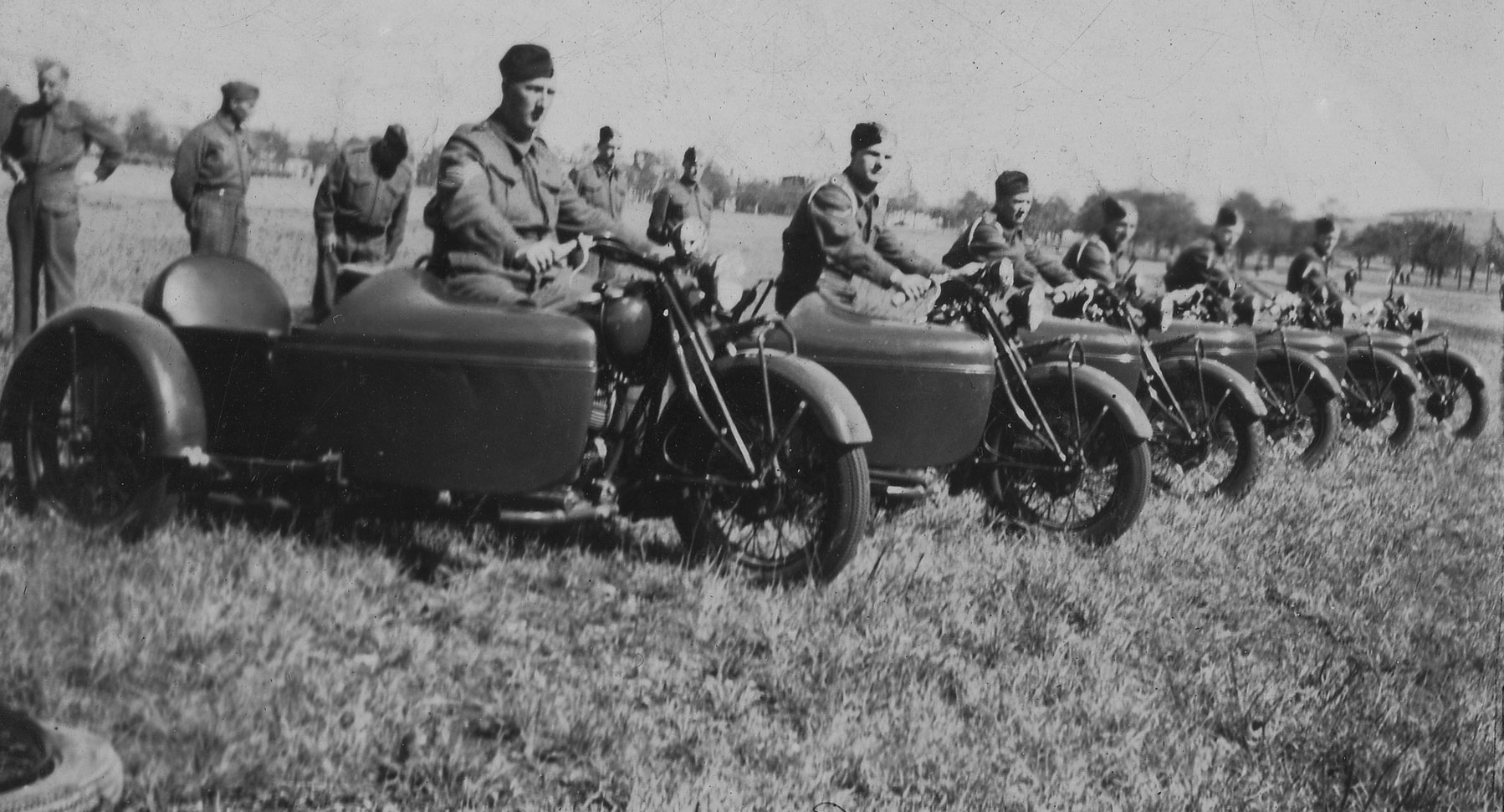 An old picture of a row of soldiers in uniform sitting on military motorcycles with sidecars.