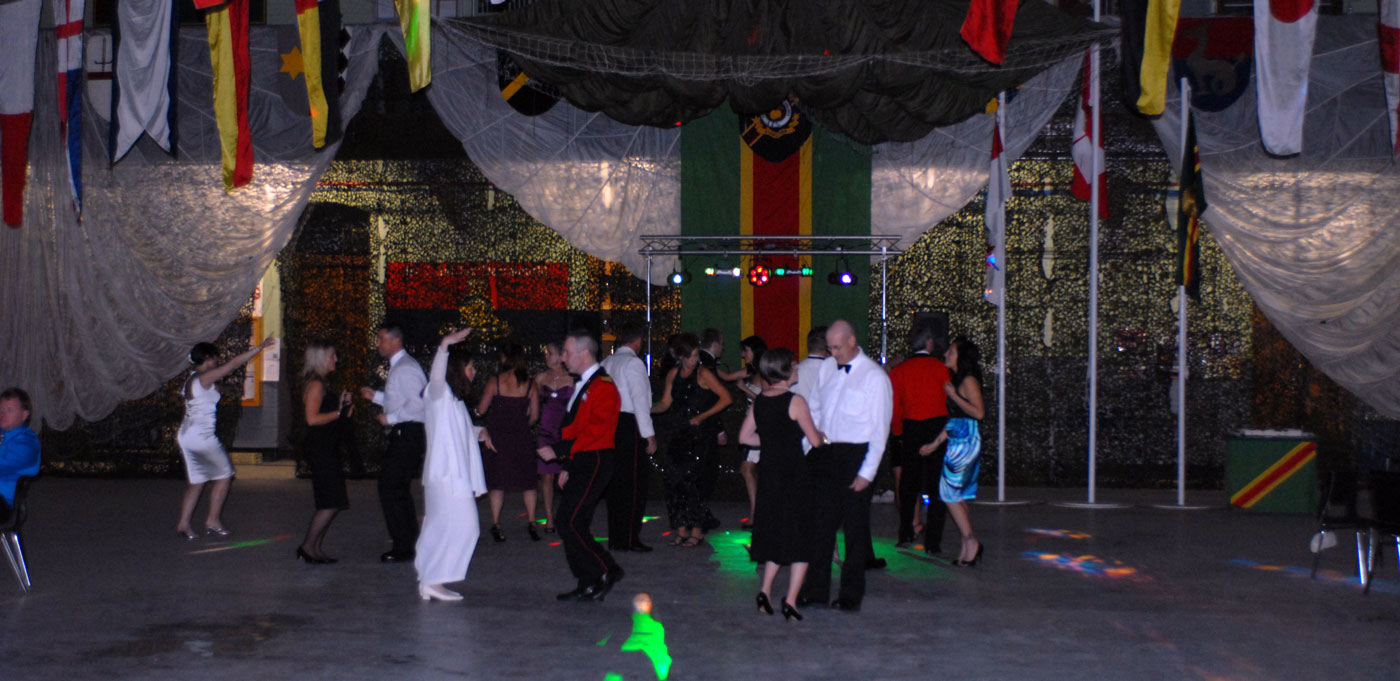 A group of people dance under colorful lights at a lively indoor party, surrounded by flags and draped fabric, creating a festive atmosphere.